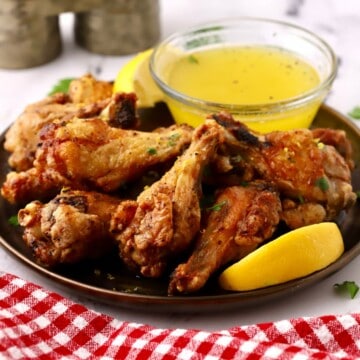 Lemon pepper chicken wings on a plate with a dipping sauce.