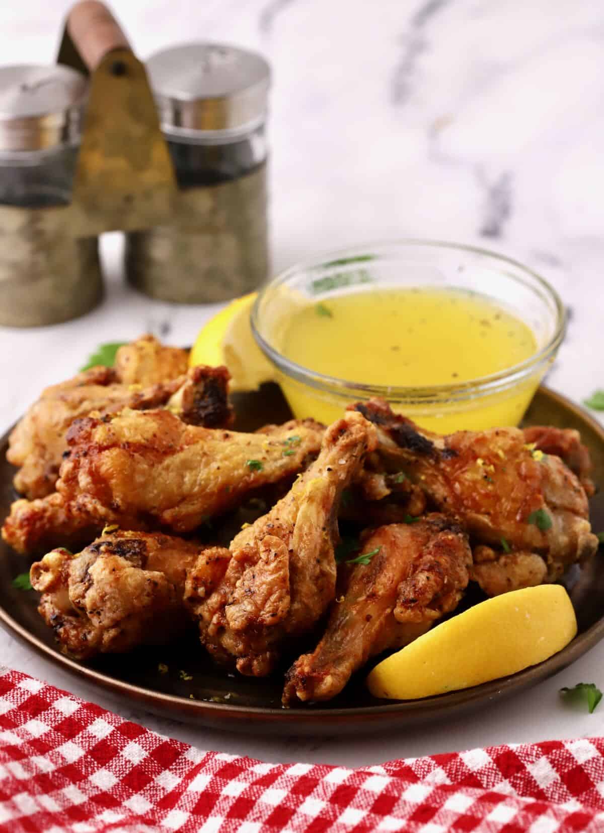 Lemon pepper chicken wings on a bronze plate with a dipping sauce.