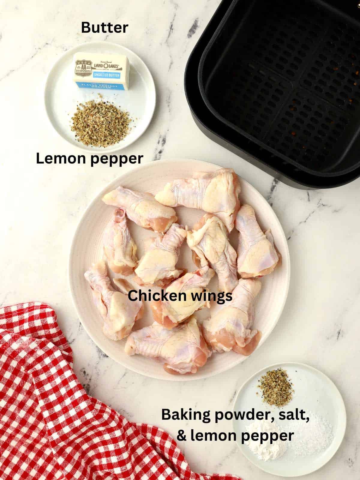 A plate of raw chicken wings with a stick of butter, and lemon pepper seasoning.