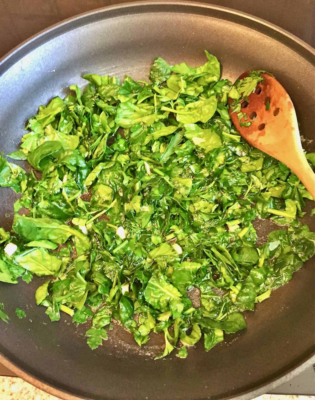 Sautéing fresh spinach in a skillet.  