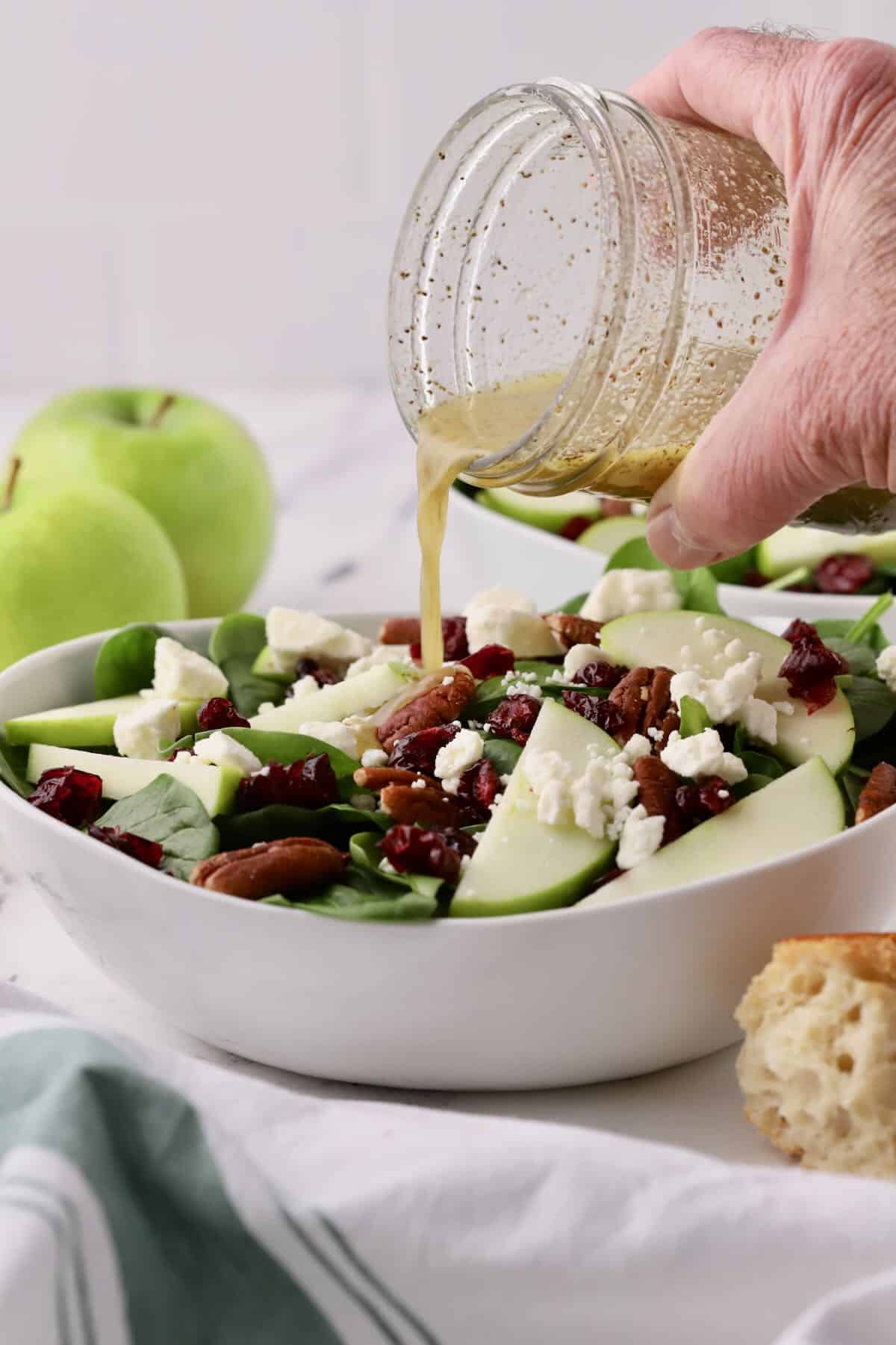 Pouring dressing out of a mason jar onto a spinach salad. 