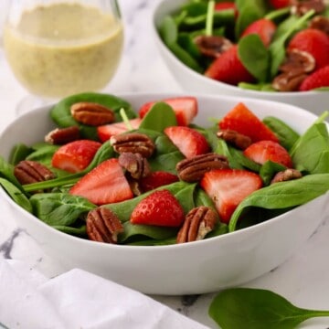 Two bowls of spinach salad and a small pitcher of poppy seed dressing.
