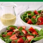 Spinach salad topped with strawberries and pecans in a white bowl.