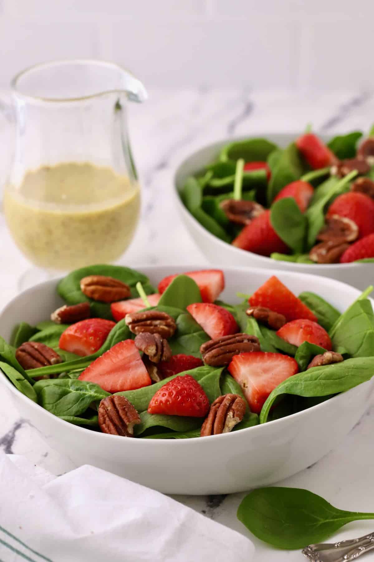 Two bowls of spinach salad topped with strawberry slices and pecans.