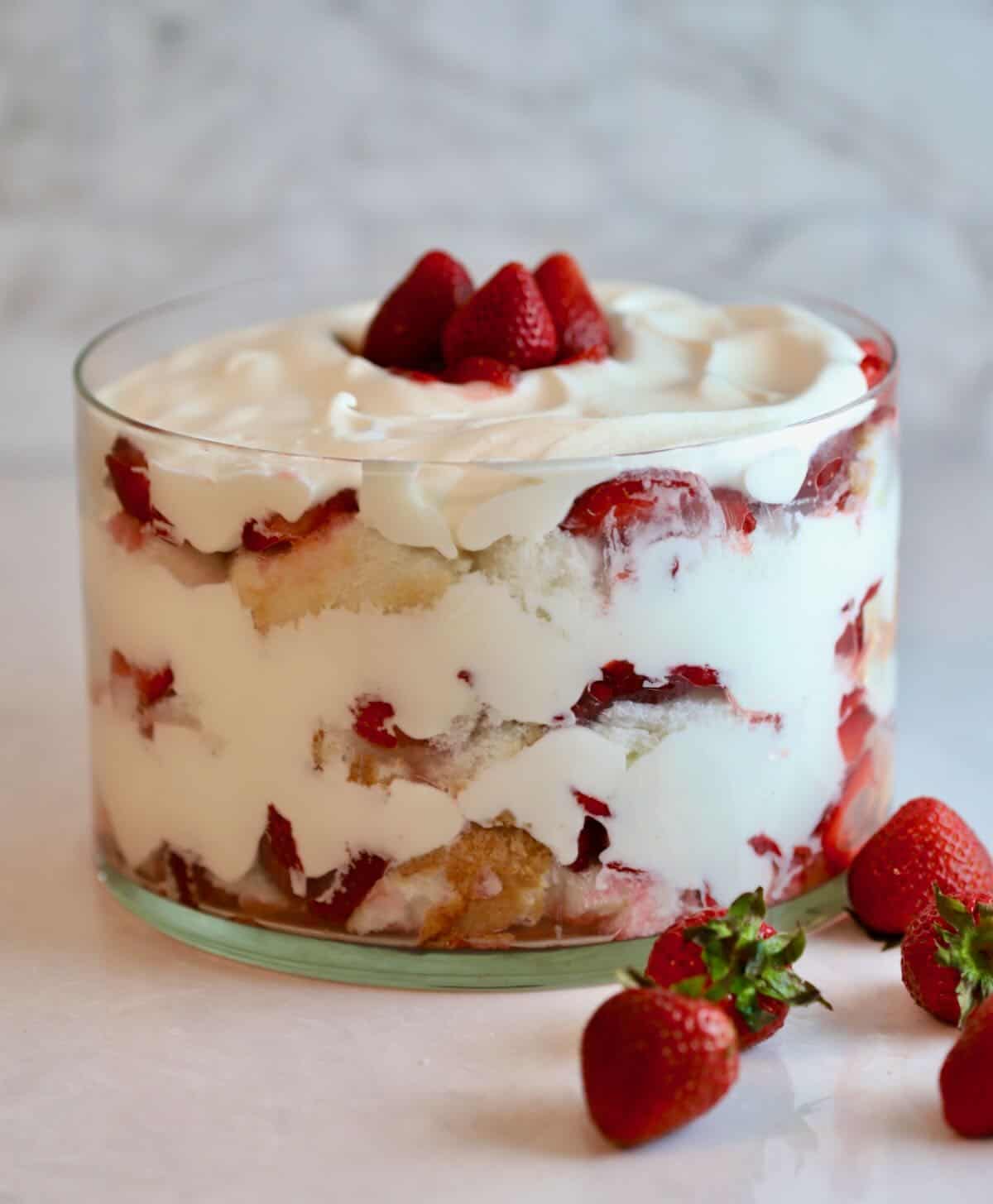 A clear glass trifle dish with layers of strawberries, whipped cream and angel food cake. 