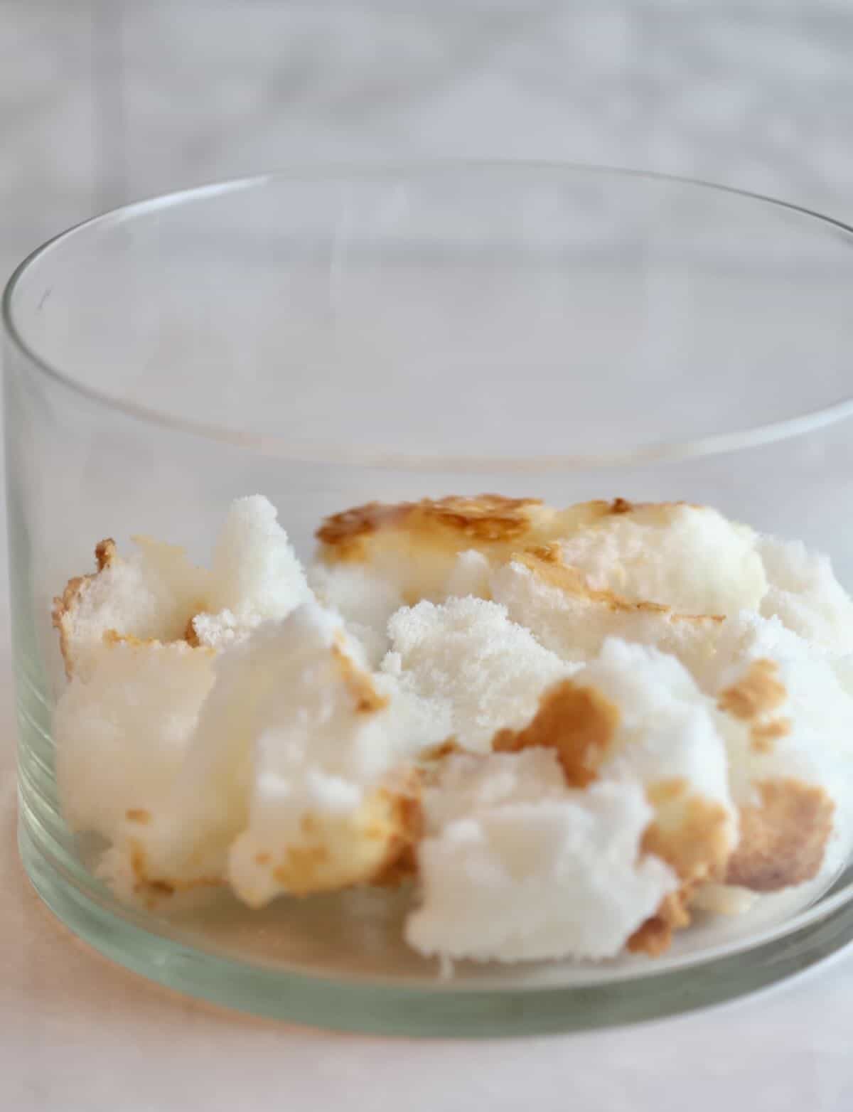 Angel food cake torn into bite size pieces in the bottom of a trifle dish.