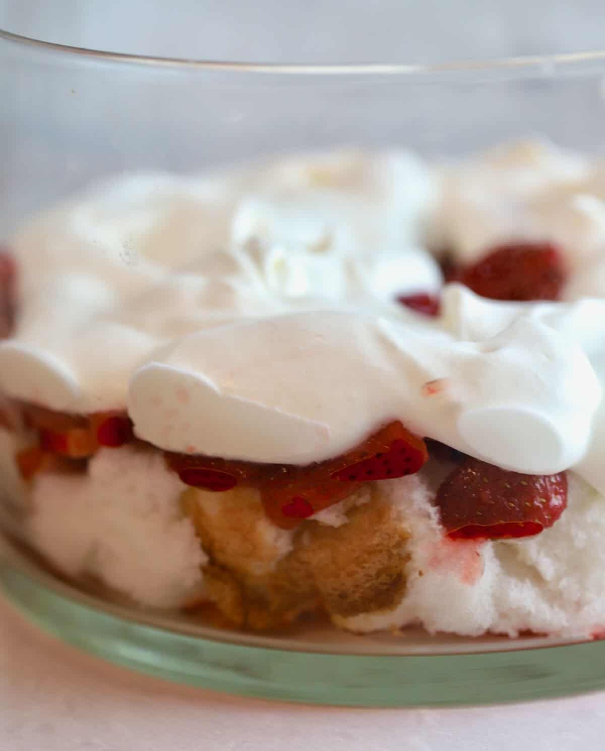 A layer of whipped cream, sliced strawberries and angel food cake in a glass trifle dish. 