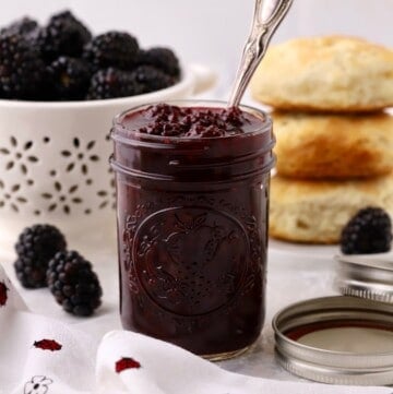 A jar of blackberry jam with a spoon sticking out.