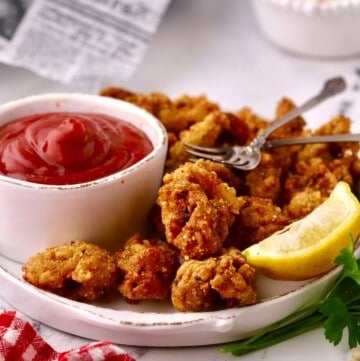 A bowl of cocktail sauce next to fried oysters on a plate.