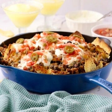 A blue enameled cast iron skillet full of nachos topped with sour cream and salsa.