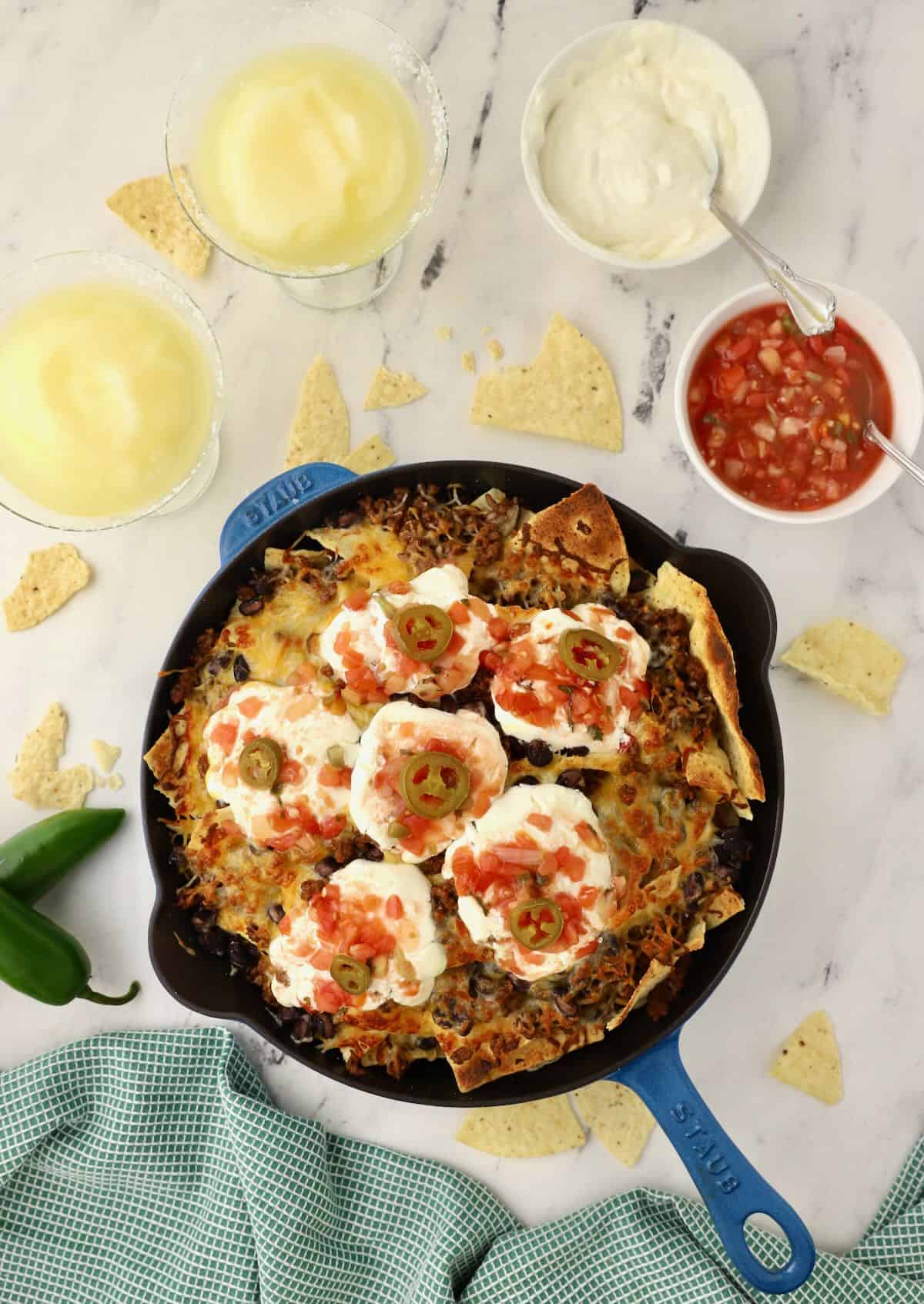 Cooked nachos in a cast iron skillet topped with sour cream and salsa. 