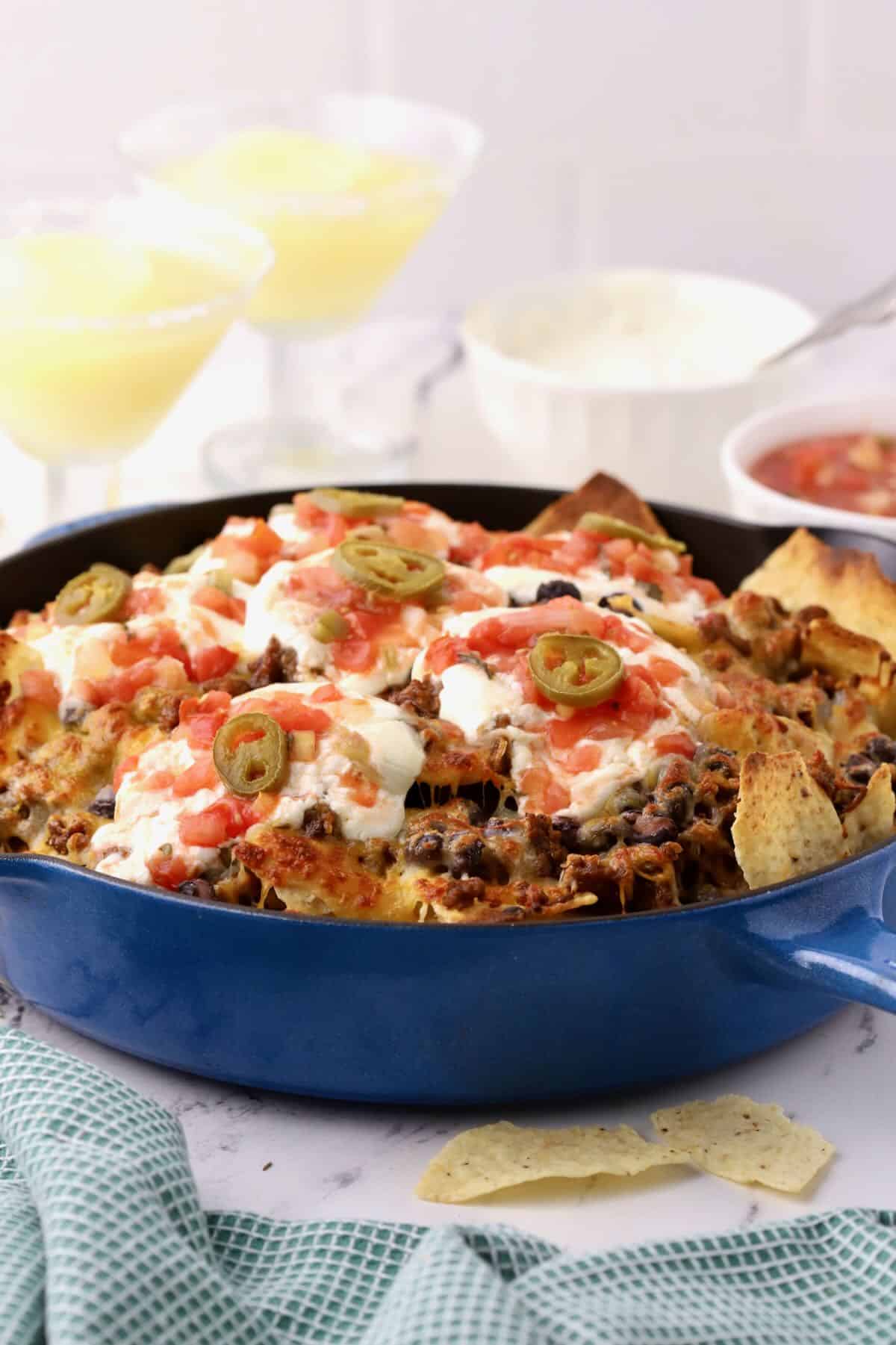 Cast iron skillet full of tortilla chips covered in melted cheese, sour cream and salsa. 