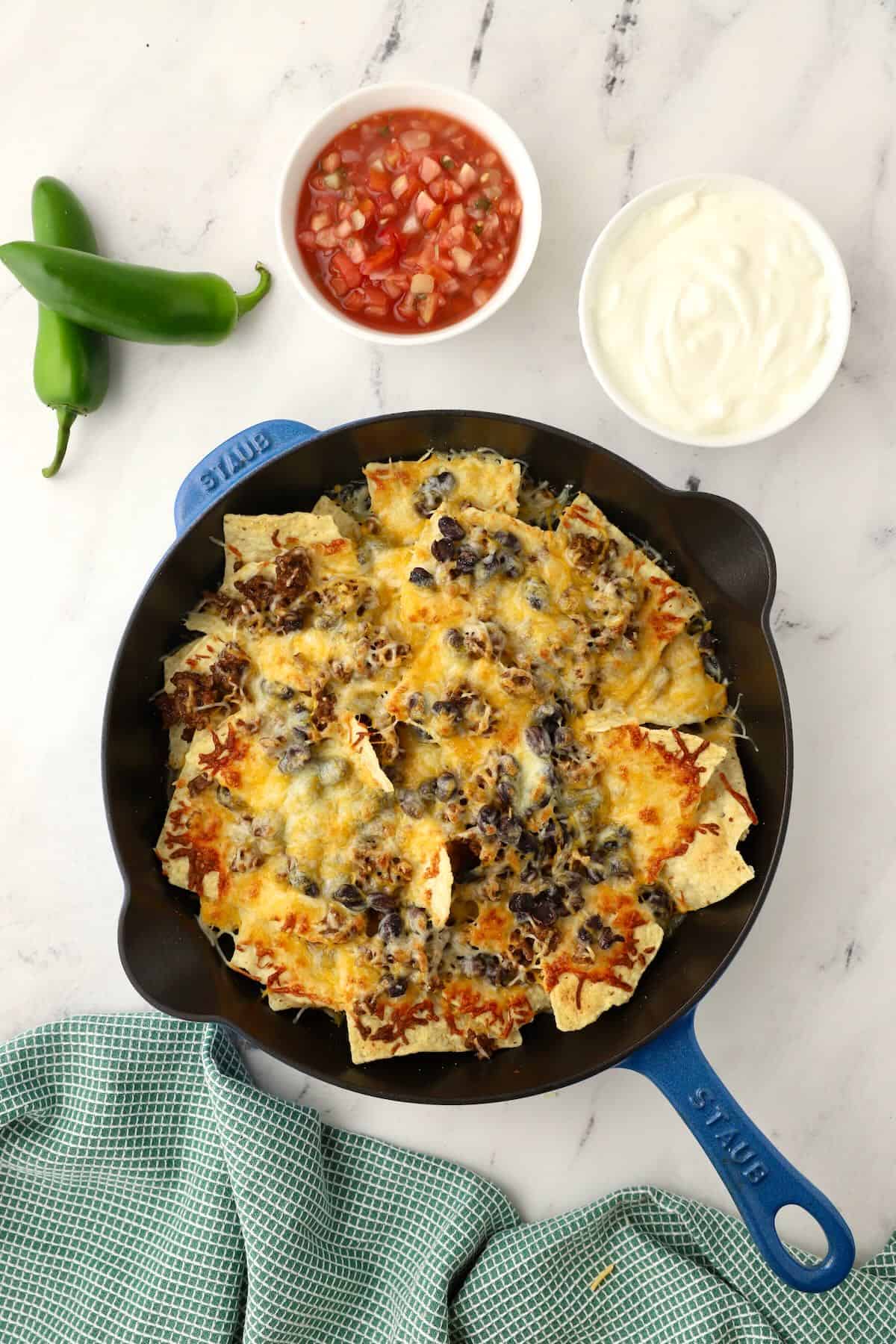 A cast iron skillet full of tortilla chips and topped with melted shredded cheese. 