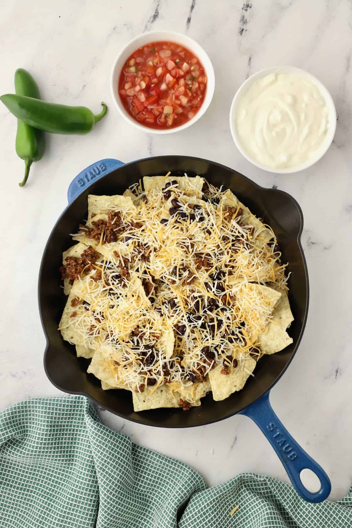 A cast iron skillet full of tortilla chips topped with shredded cheese. 