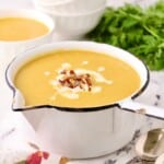A large white saucepan full of pureed sweet potato and carrot soup, garnished with pecans.