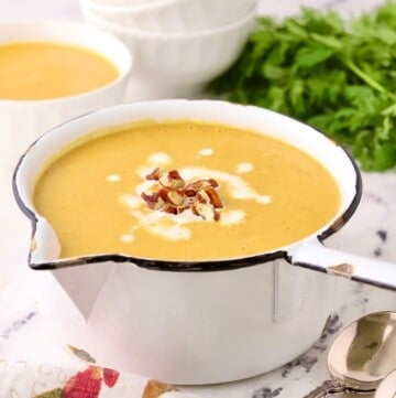 A large white saucepan full of pureed sweet potato and carrot soup, garnished with pecans.
