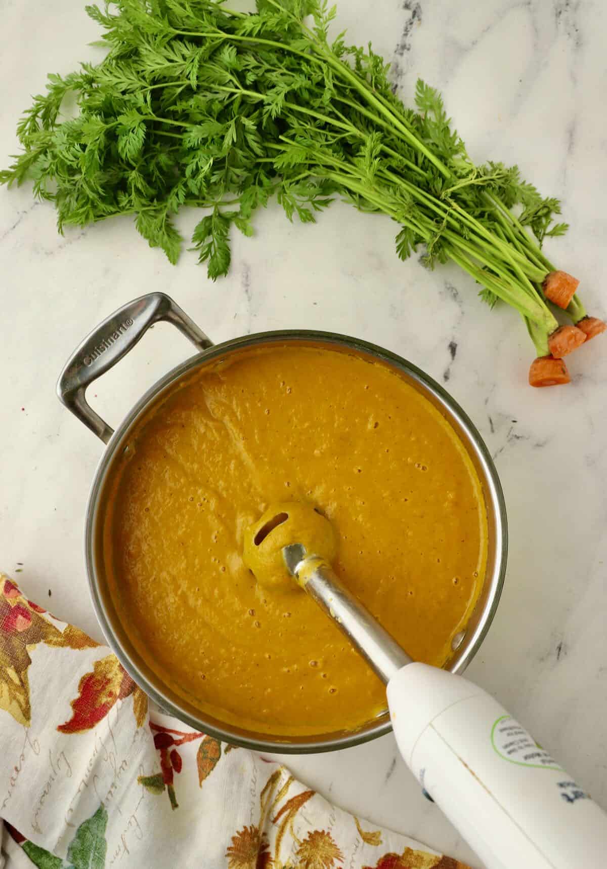 Using an immersion blender to puree soup until smooth. 