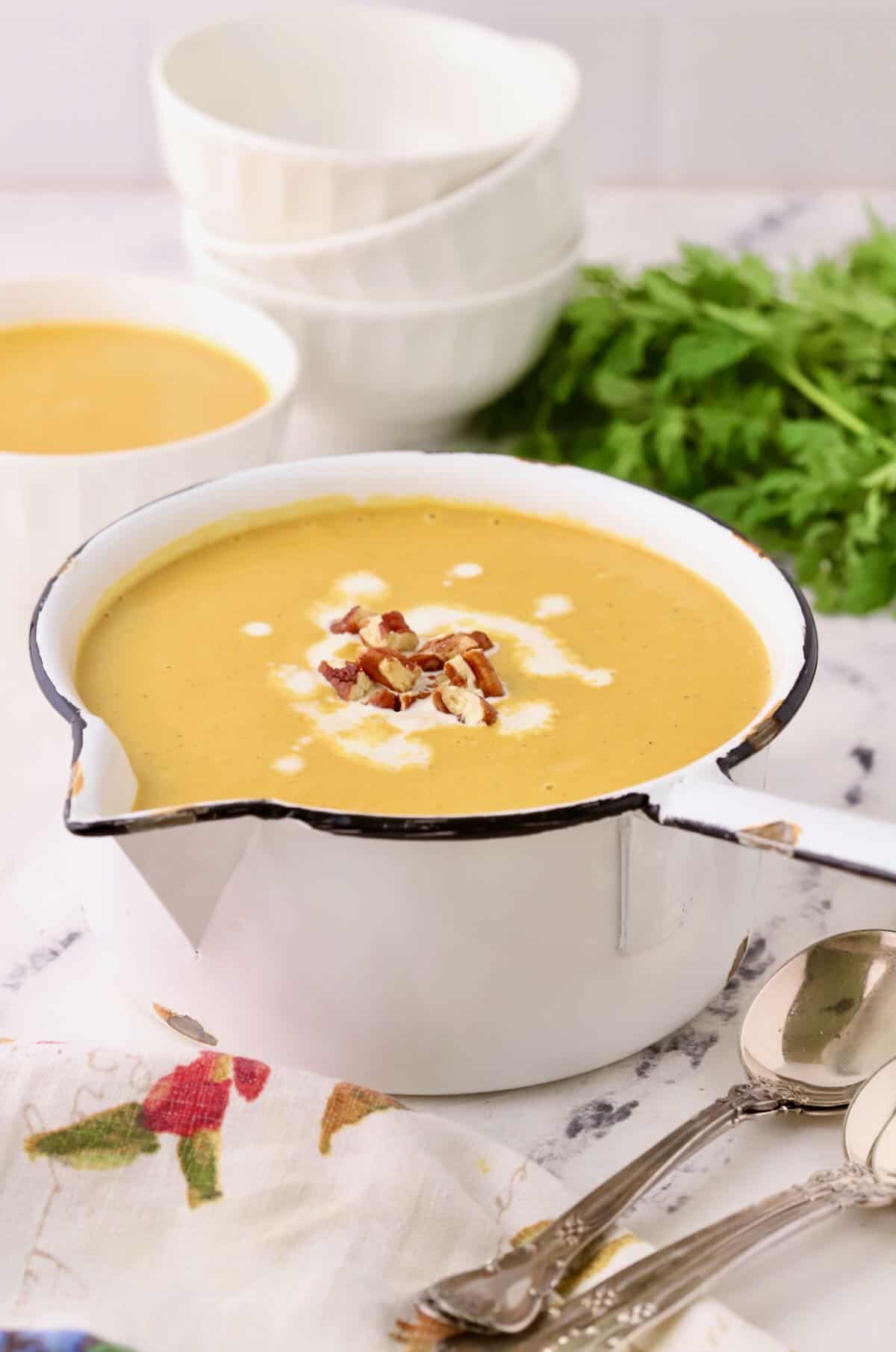 A white saucepan full of sweet potato carrot soup, garnished with pecans.