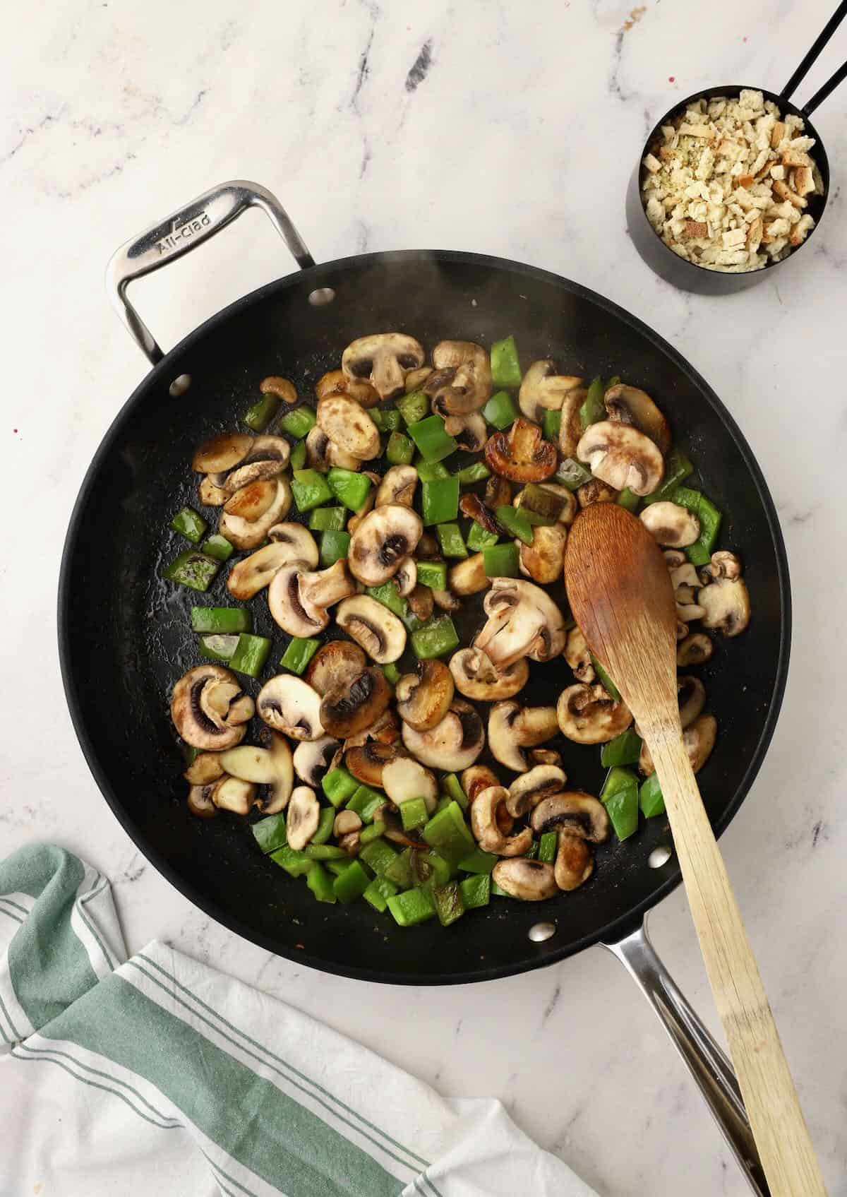 Sliced mushrooms and bell pepper cooking in a skillet. 