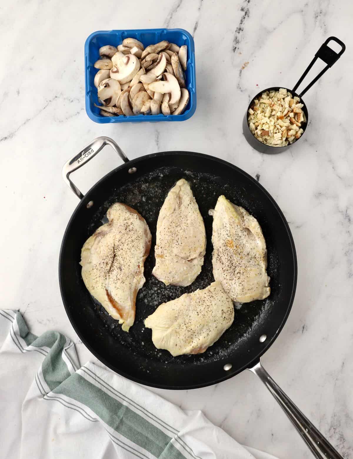 Four chicken breasts cooking in a skillet. 