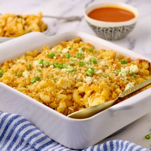 A white square baking dish full of buffalo chicken pasta topped with panko and scallions.