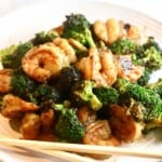 Stir-fried shrimp and broccoli on a white plate with chop sticks.
