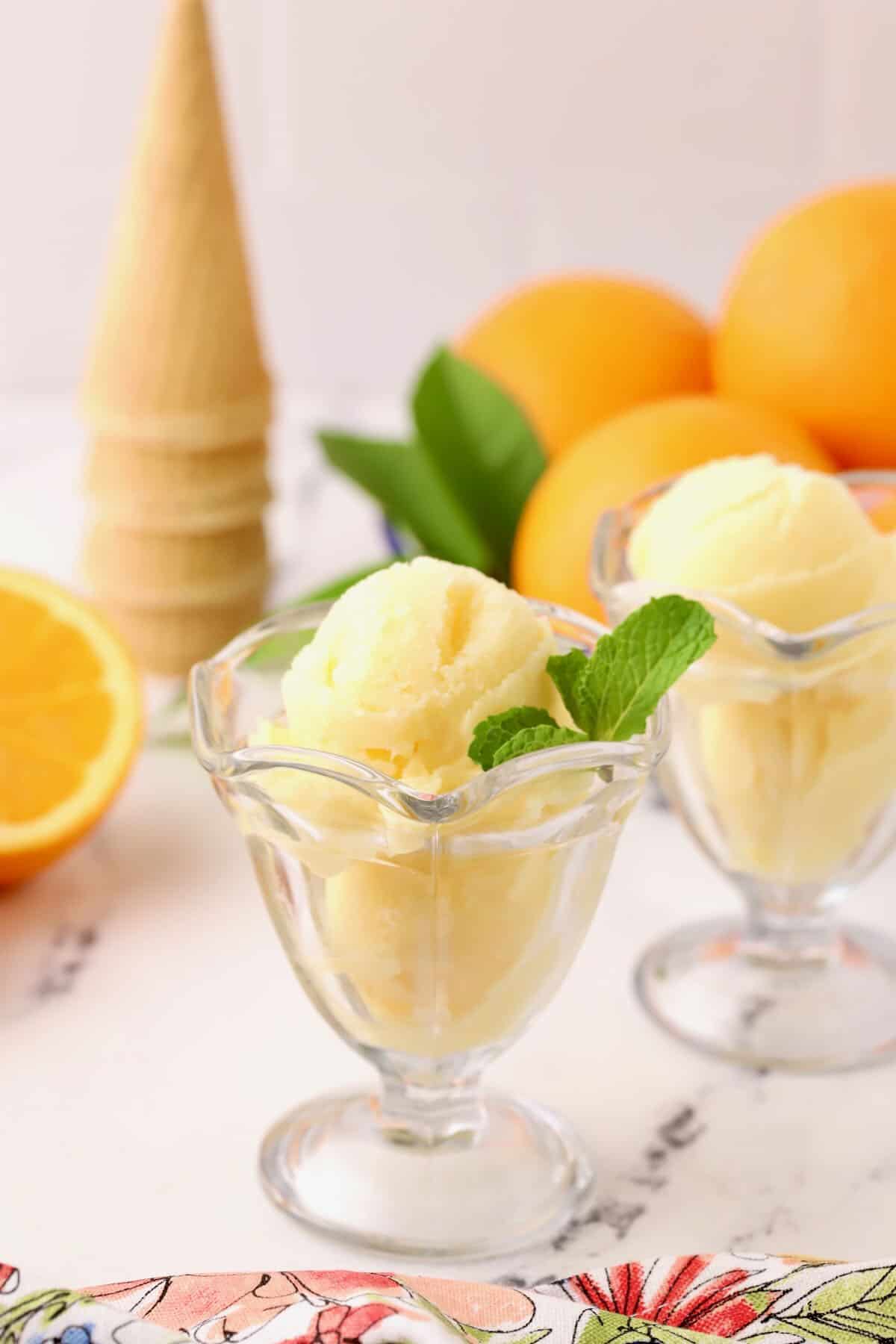 Two scoops of orange sherbet in a glass dish. 