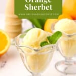 A clear dessert dish with two scoops of orange sherbet garnished with a sprig of mint.
