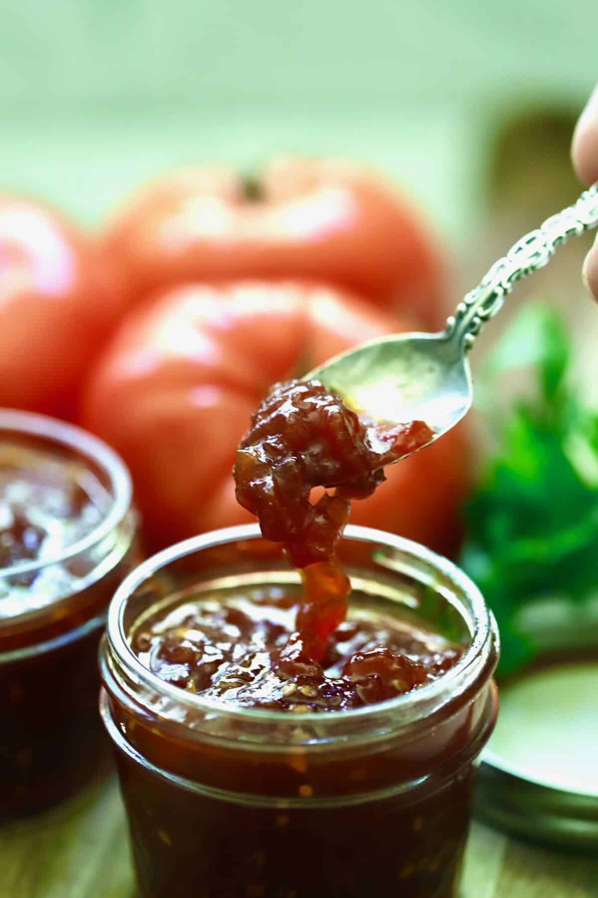 A jar of tomato jam with a spoon full of it. 