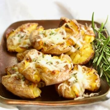 Smashed truffle potatoes on a bronze plate with a sprig of rosemary.