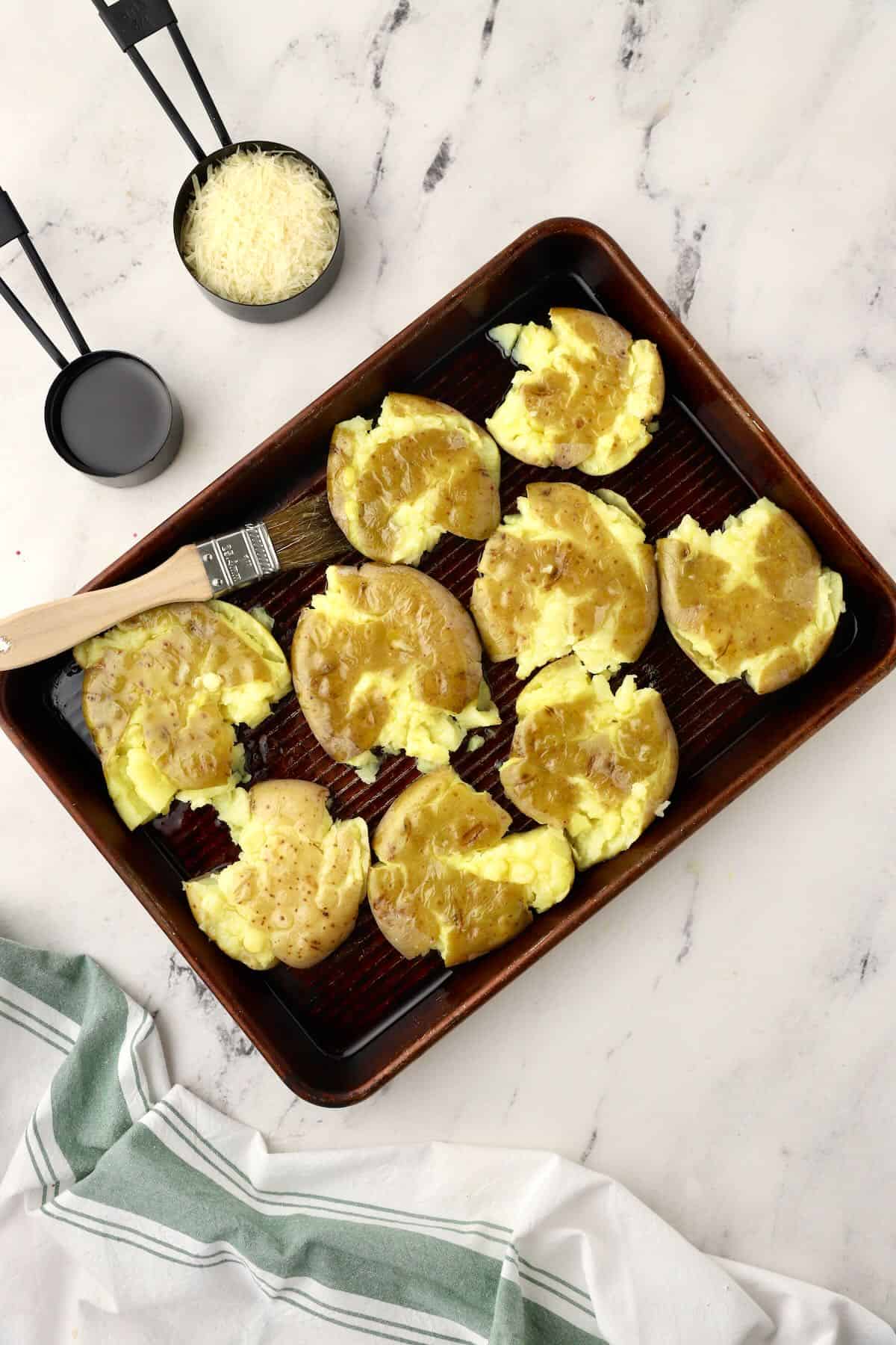 Brushing olive oil on smashed potatoes on a baking sheet. 