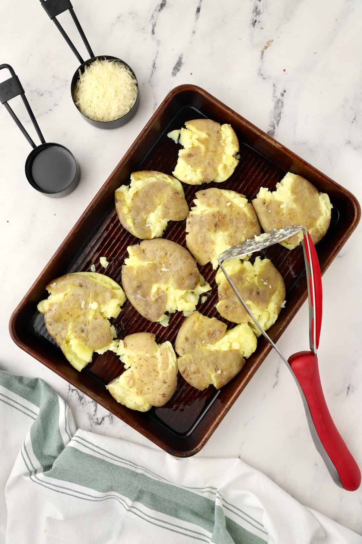 Small potatoes smashed with a potato masher on a baking sheet. 