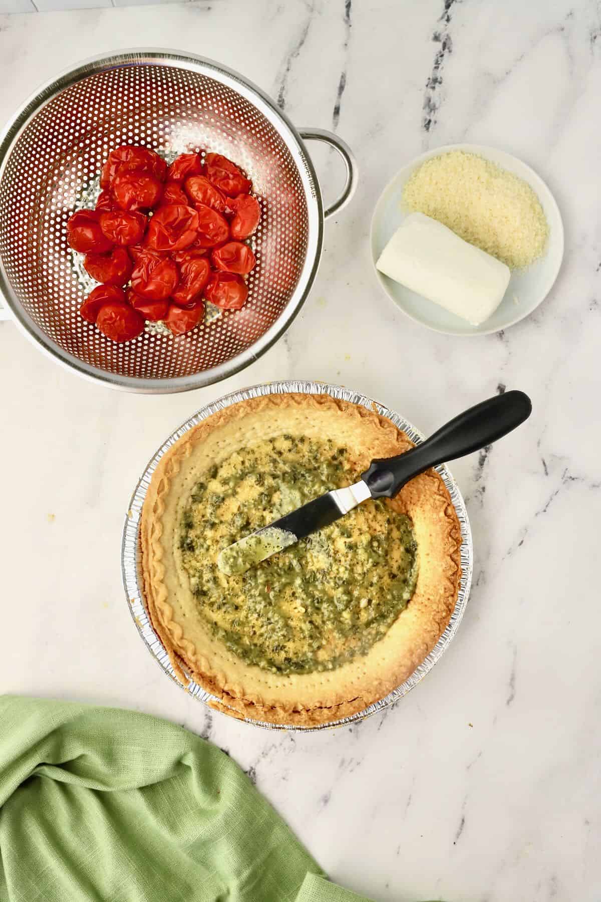 An offset spatula spreads pesto on the bottom of a pie crust. 