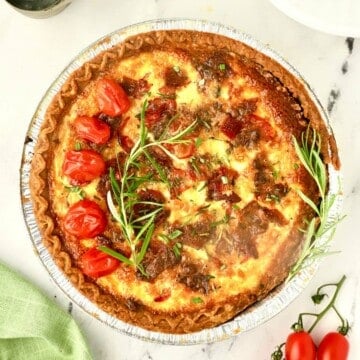 Breakfast quiche with goat cheese, garnished with roasted tomatoes and rosemary.
