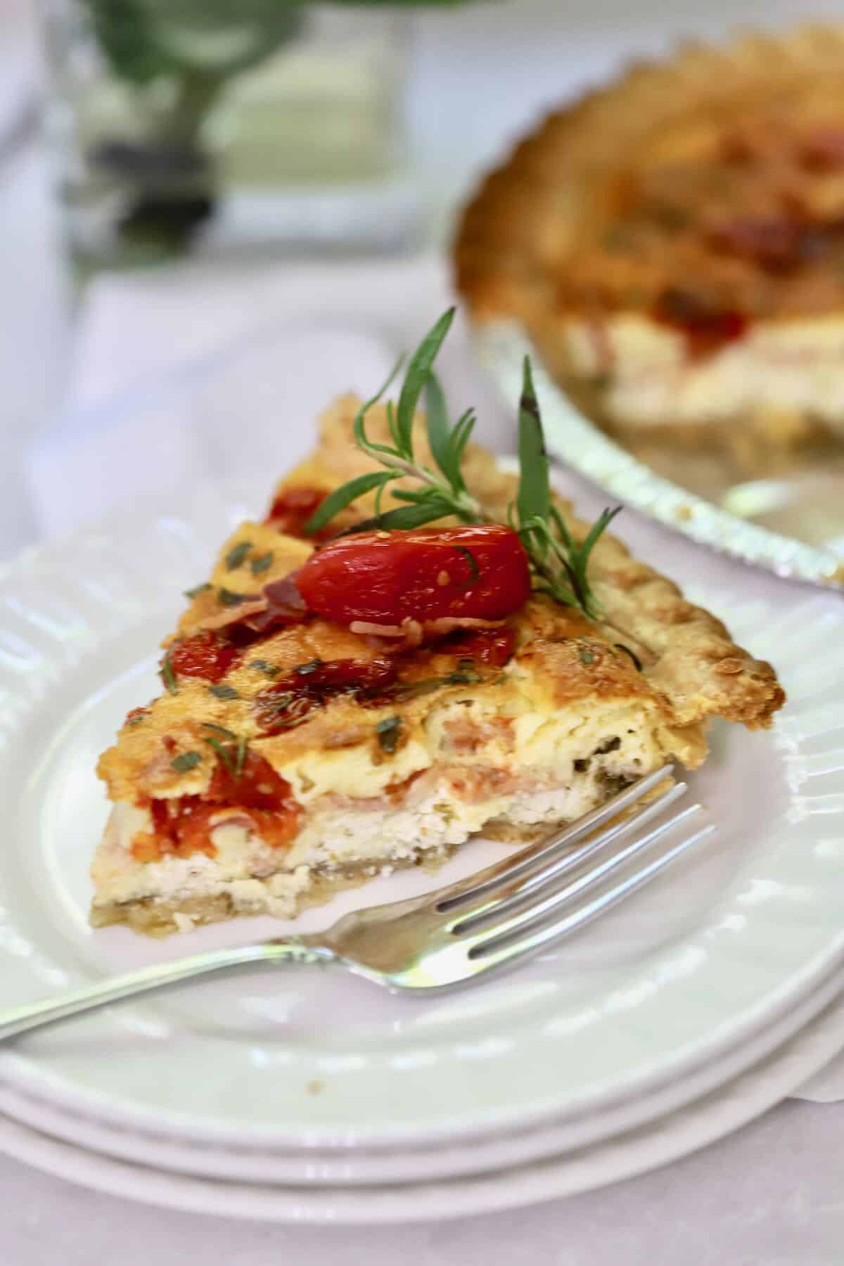 A slice of quiche topped with roasted tomatoes and fresh rosemary.