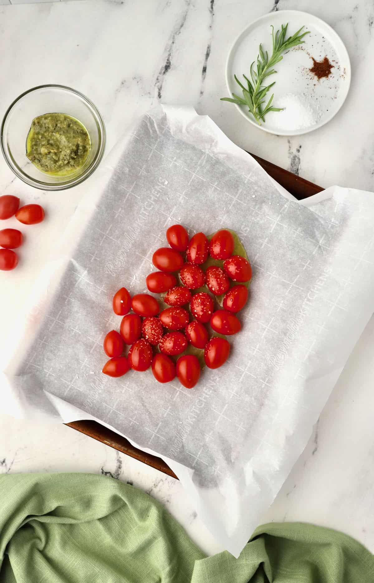 A baking sheet covered with parchment paper topped with cherry tomatoes. 