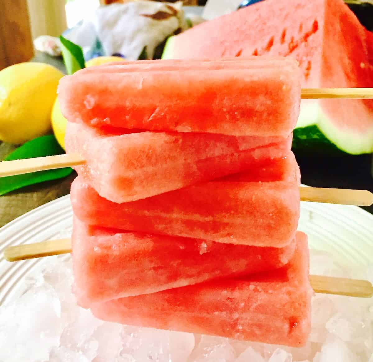 A stack of watermelon popsicles on a plate filled with ice. 