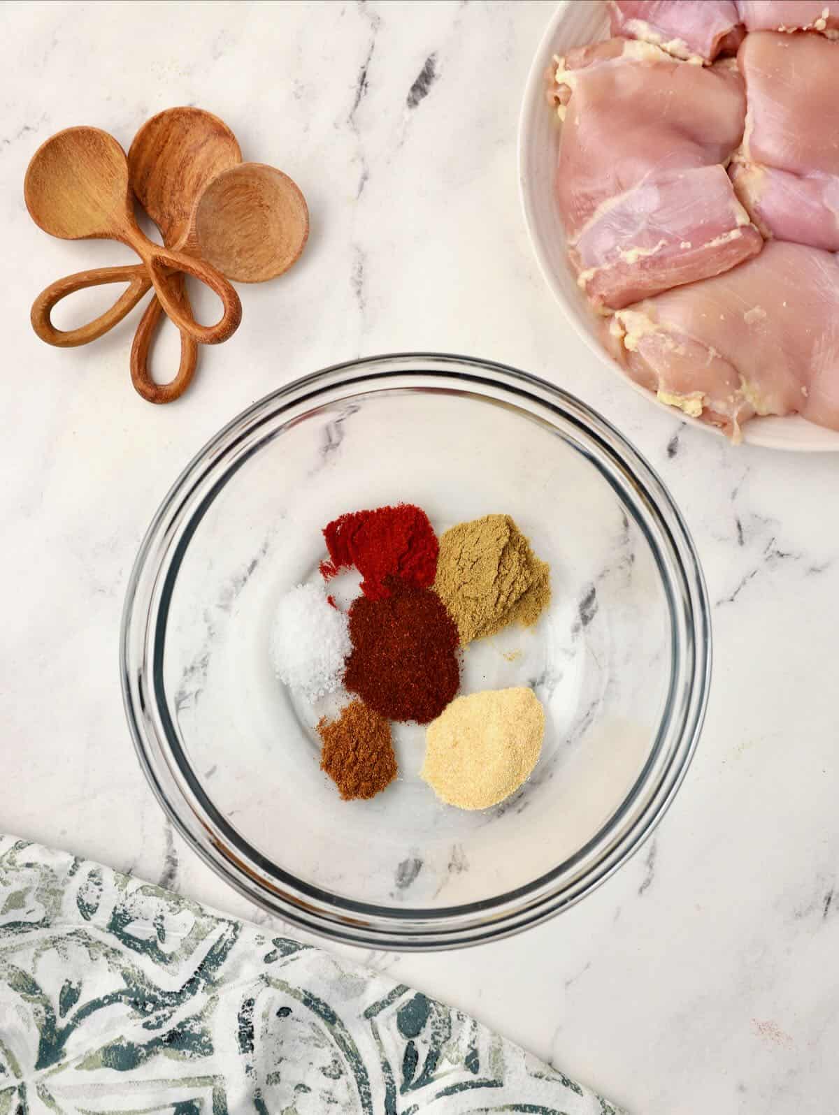 Spices including paprika, cumin, garlic powder, and chili powder in a clear glass bowl. 