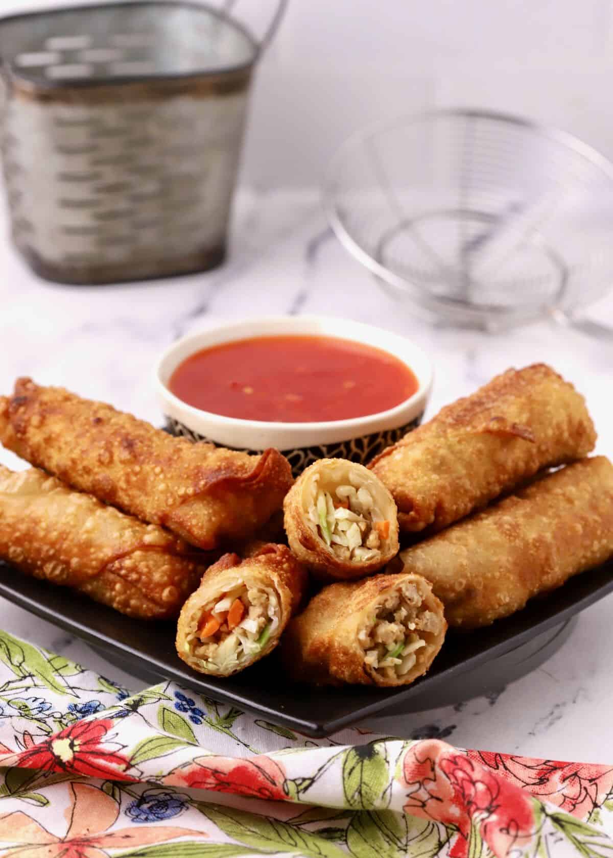 Chicken egg rolls on a black plate with a bowl of dipping sauce. 
