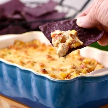 Using a blue corn chip to scoop a serving of hot corn dip with cream cheese.