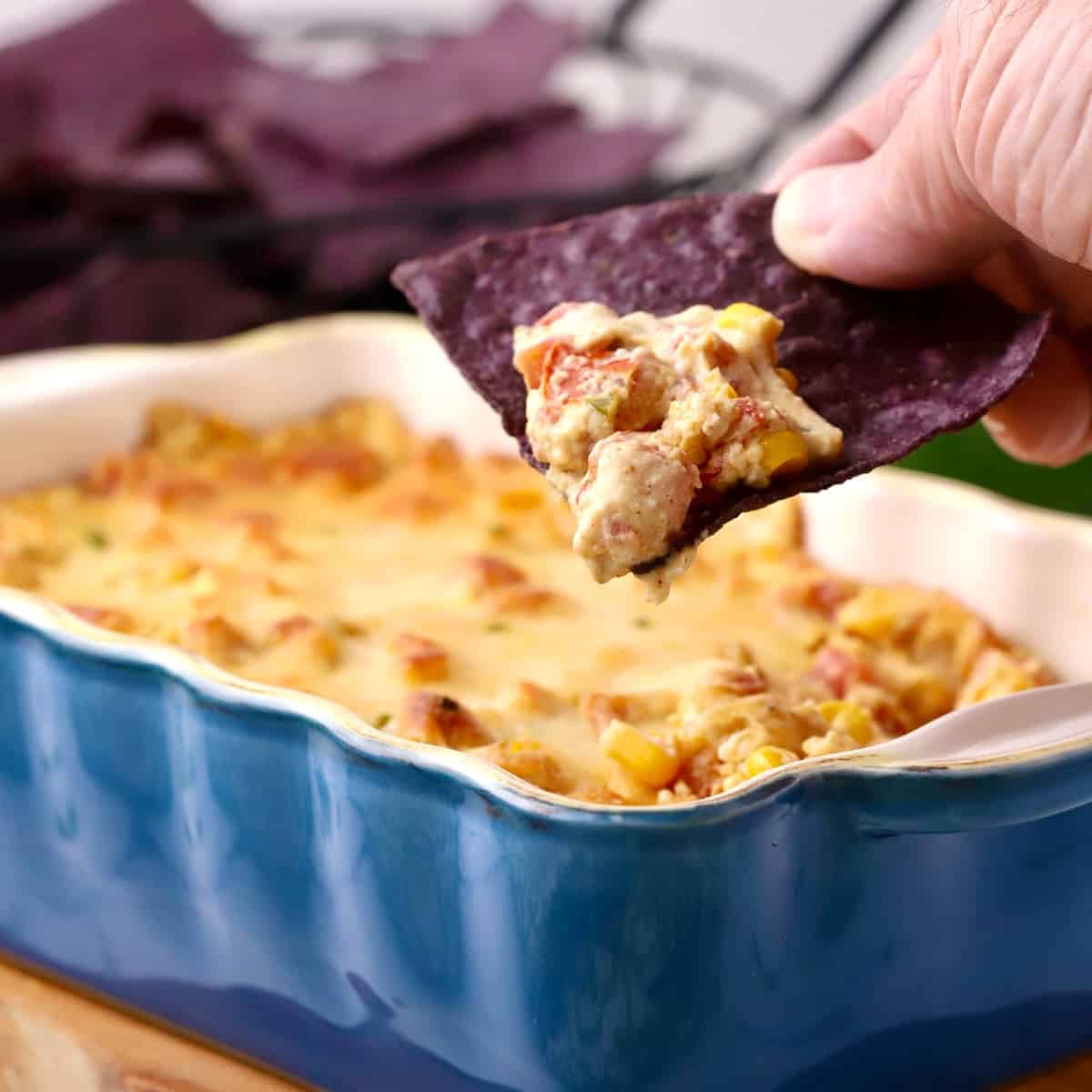 Using a blue corn chip to scoop a serving of hot corn dip with cream cheese.