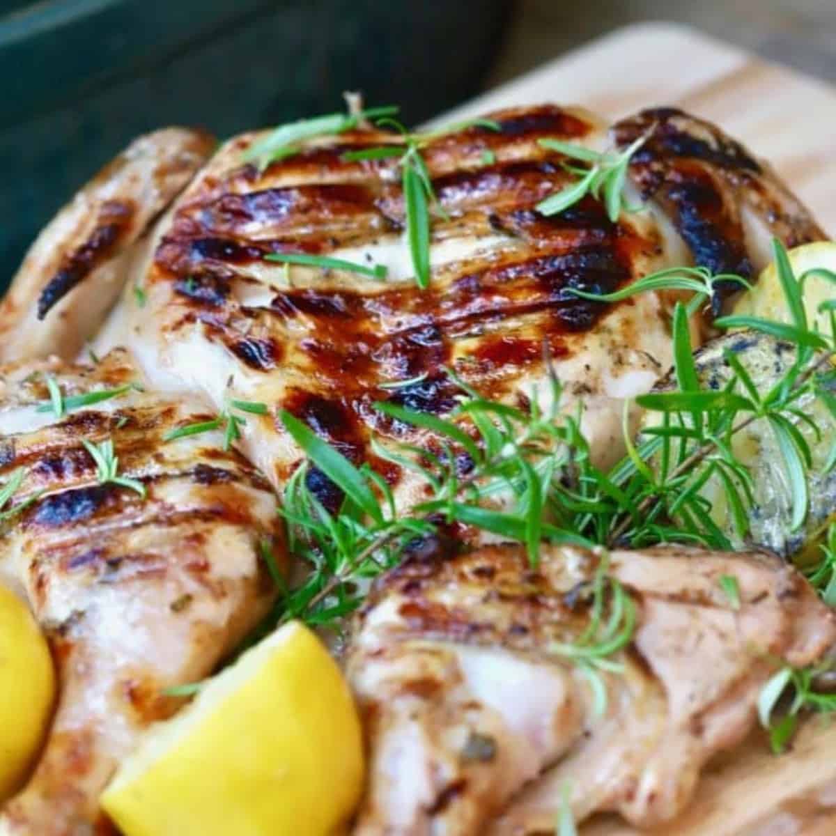 Grilled spatchcock chicken topped with sprigs of rosemary and sliced lemons.