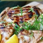 A grilled spatchcock chicken garnished with a lemon and sprigs of rosemary.