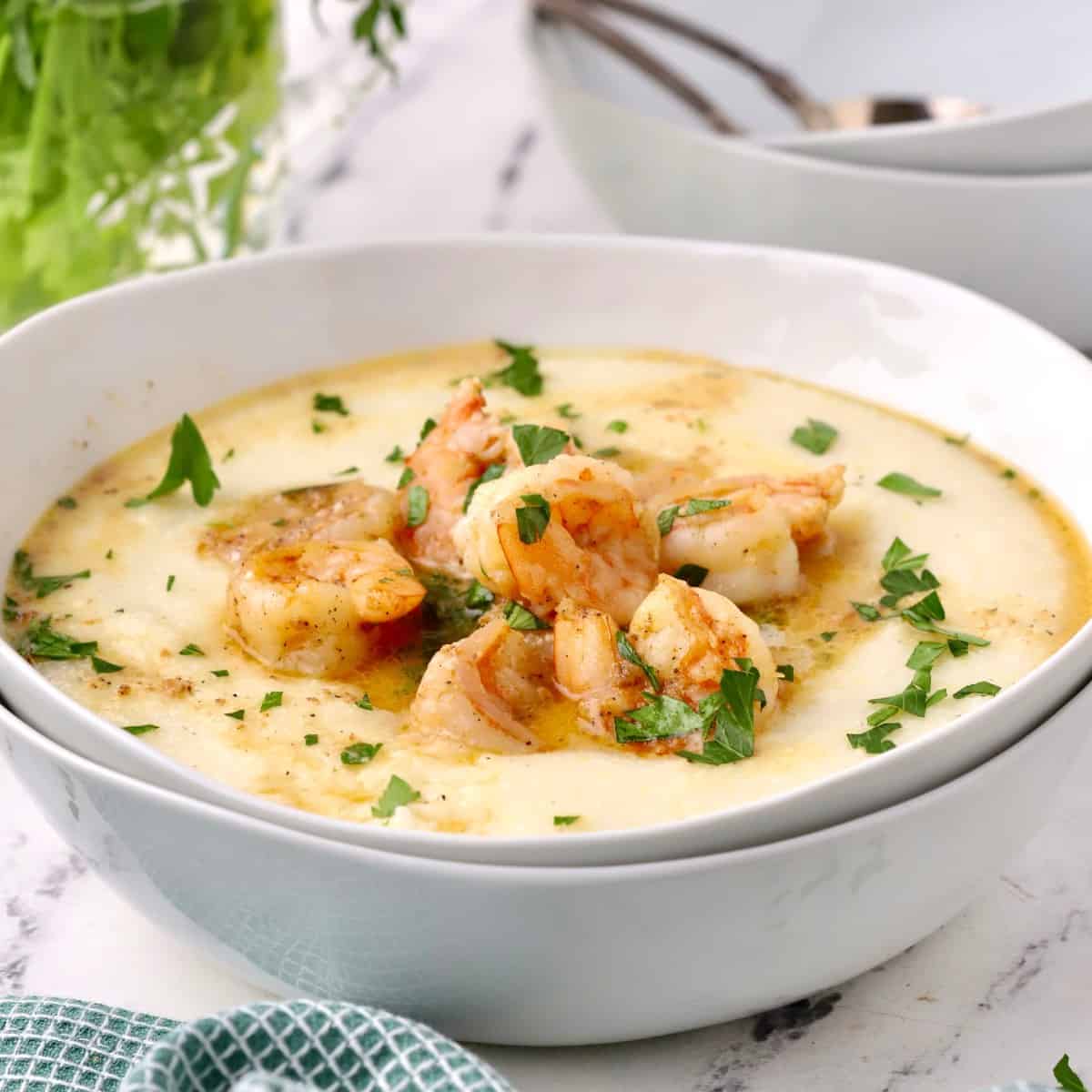 Cajun shrimp and grits in a white bowl garnished with chopped parsley.