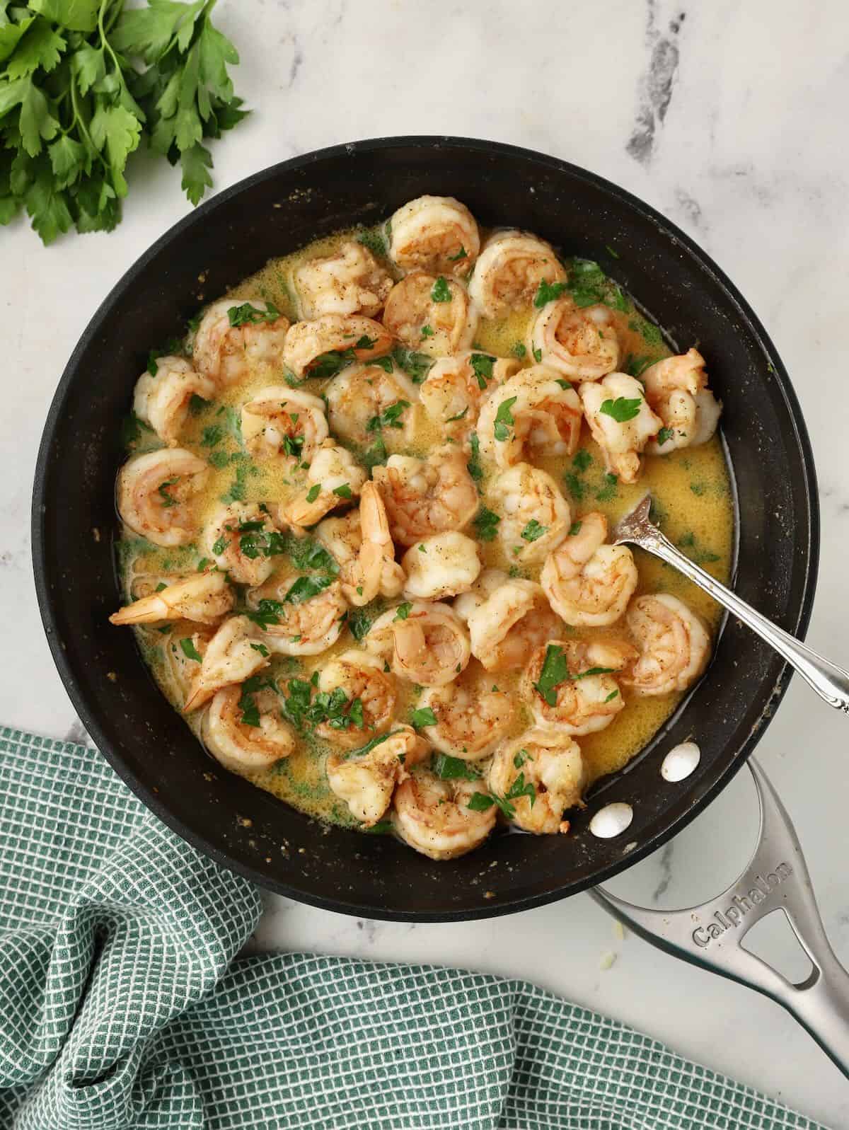 Cooked shrimp in a skillet with a lemon garlic sauce, topped with parsley. 