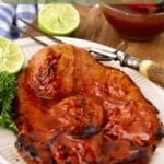 A grilled ham steak covered in glaze on a white serving plate.
