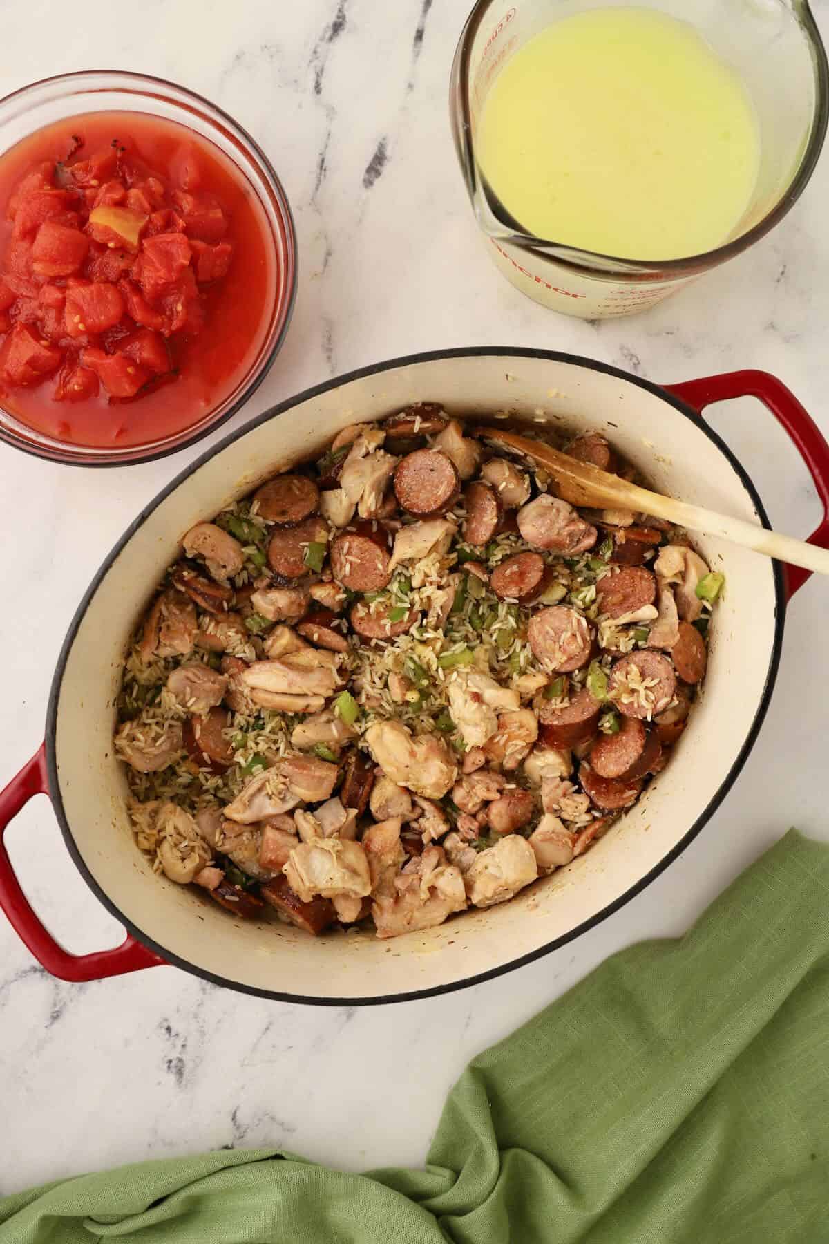 Cooked sausage and chicken added to vegetables and rice in a pan.