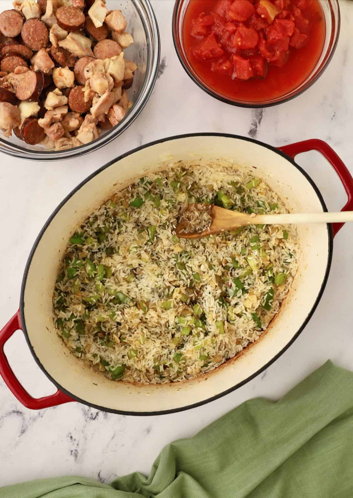 Uncooked rice added to chopped vegetables and seasoning in a Dutch oven. 