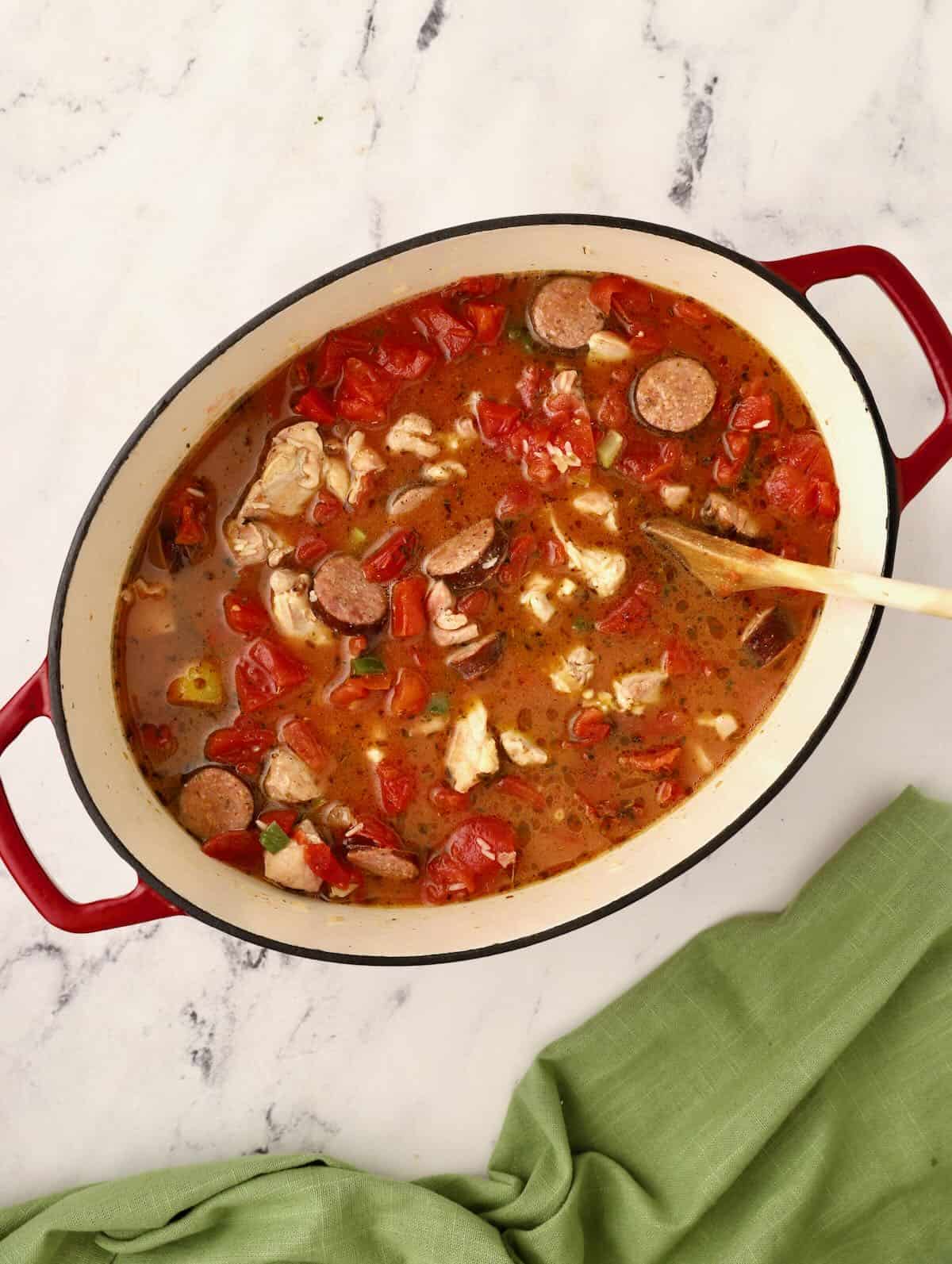 Jambalaya cooking in a Dutch oven with canned tomatoes. 