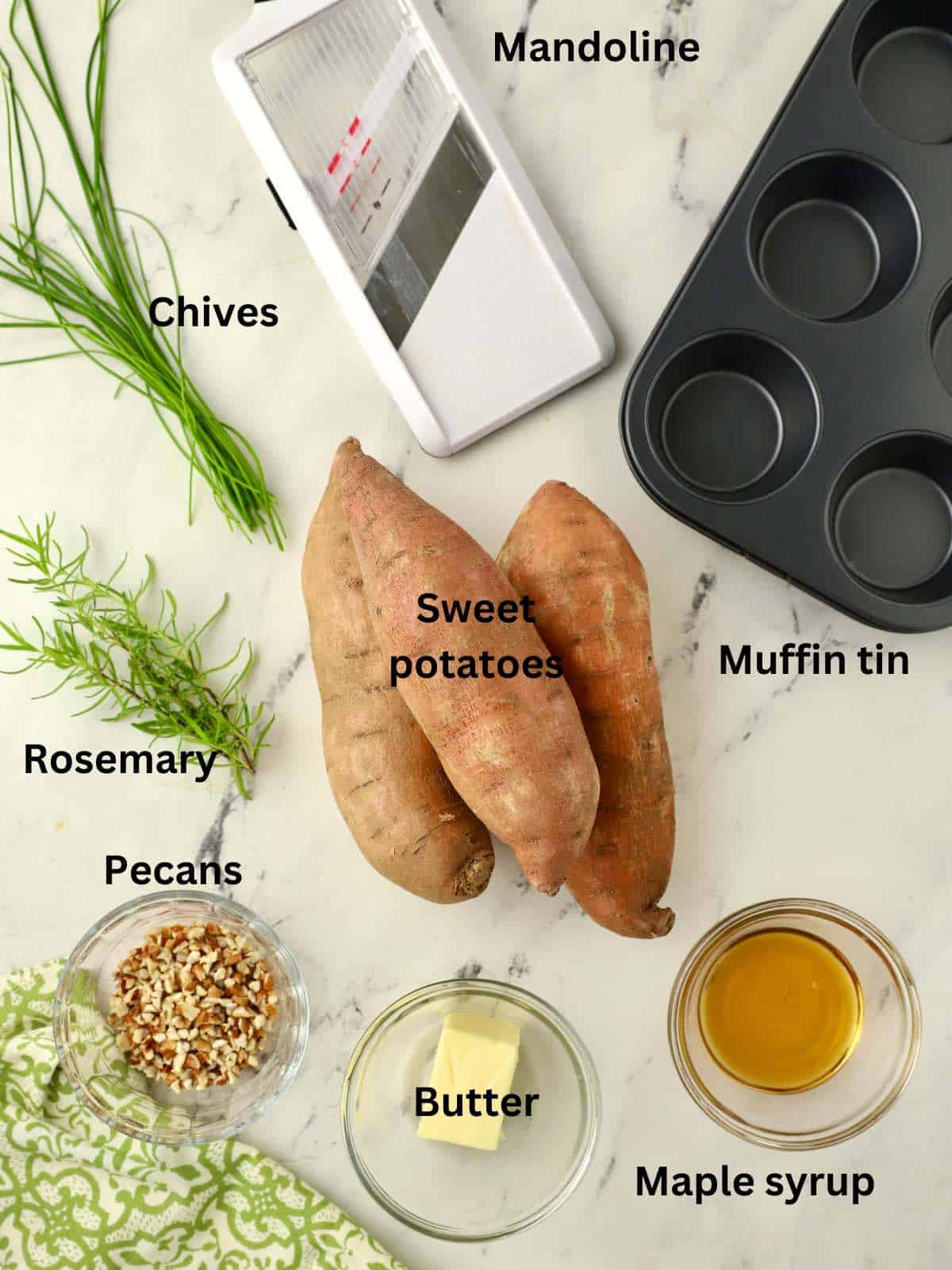 Sweet potatoes, herbs, butter, and a mandoline on aa cutting board. 